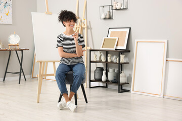 Young woman with brush palette near easel in studio