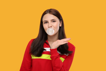 Beautiful woman blowing bubble gum on orange background