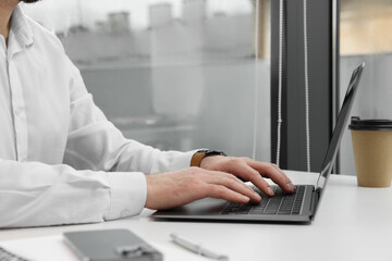 Man working on laptop at white desk in office, closeup