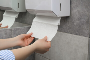 Woman taking new fresh paper towel from dispenser in bathroom, closeup