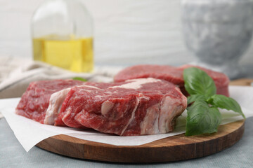 Fresh raw cut beef and basil leaves on grey table, closeup