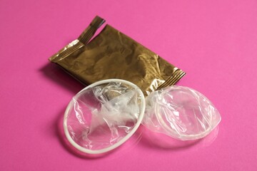 Unrolled female condom and torn package on pink background, closeup. Safe sex