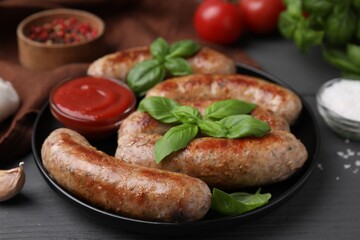 Tasty homemade sausages, ketchup and basil leaves on grey wooden table, closeup