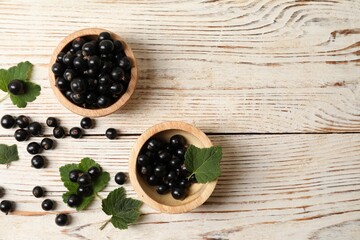 Ripe blackcurrants and leaves on light wooden table, flat lay. Space for text
