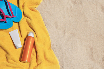 Sunscreens, flip flops and towel on sand, top view with space for text. Sun protection care