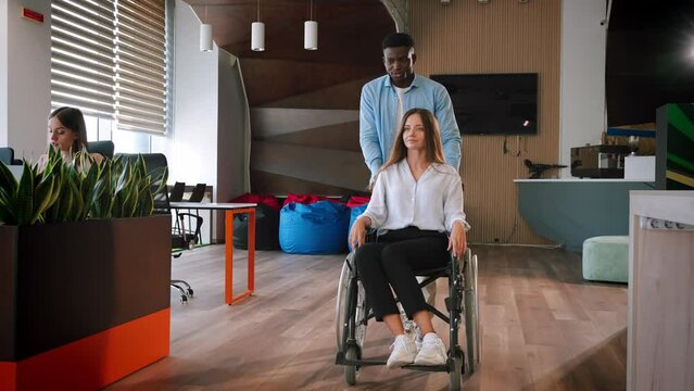 African American man talks to lady colleague pushing wheelchair
