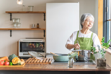 家のキッチンで料理を作るアジア人のシニア・高齢者女性（笑顔）
