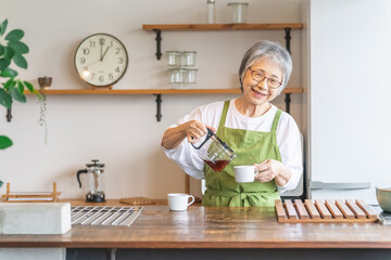 家・カフェのキッチンでコーヒーを淹れるアジア人高齢者女性
