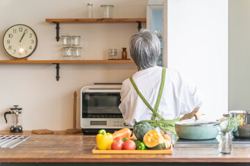 家のキッチンで料理を作るため冷蔵庫から野菜を出すアジア人の高齢者女性
