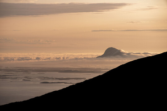 Mountain islands in Norwegian archipelago of Helgeland during sunset. Clouds forming on island mountain peaks at sea. Yellow sunset nordnorge. Dramatic contrast in Norway peaks. Smaltind, Lur&ouml;y fjell