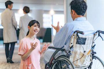 病院で車椅子の患者と会話する看護師