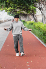 Asian sportsman is skipping rope outdoors in the city. 