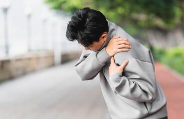 Asian man is suffering from shoulder pain with hand covering on it. 