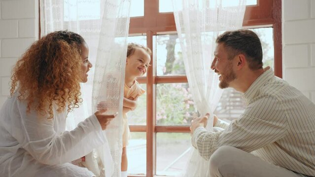 Cheerful parents playing with daughter together in living room at home. Father and mother take care give time to little baby in bedroom at house. Family relationship concept.