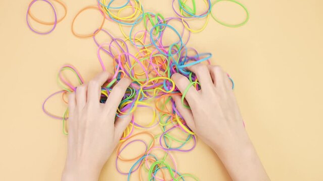 Hands taking bunch of colorful rubber bands and squizzing them on yellow background. Bright office rubber bands. Multicolored elastic rubber bands close up.