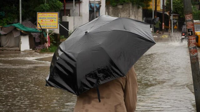A person walks on the street with a black umbrella to shield themselves from rain