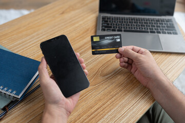 Young asian businessman holding credit card and using mobile phone, laptop for digital banking, internet payment, online shopping via mobile app, financial technology, ecommerce concept