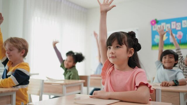 Elementary students raising hands to answer question from teacher in the classroom at school