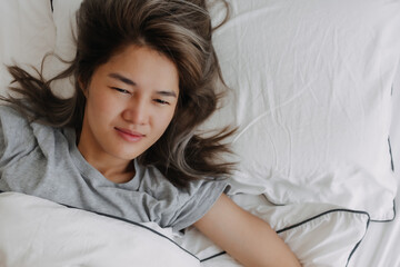 Top view of asian woman just wake up lying on the bed feeling not ready. High quality photo