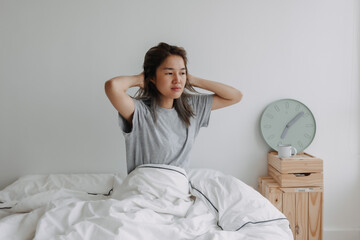Asian woman just wake up by the clock at 7 AM on the bed in the morning.