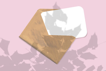 An envelope with sheet of textured white paper on pink table background. Mockup with an overlay of tropical plant shadows. Natural light casts shadows from the leaves of a tree branch. Horizontal