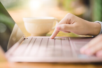 Young woman sitting in coffee shop at wooden table, drinking coffee and using laptop.