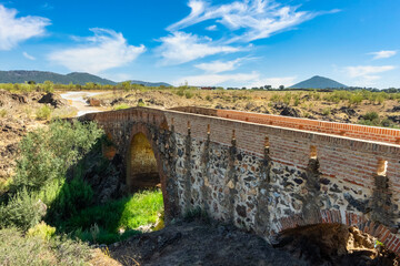Fototapeta na wymiar Roman stone bridge that crosses a small stream that leads to the summit of the nearby mountains, Agudo, Ciudad Real.