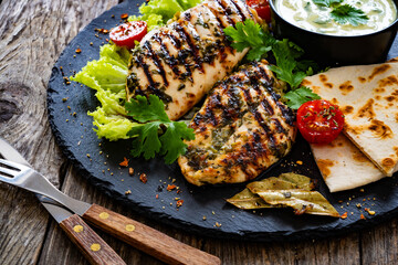 Grilled chicken breast, pita bread and fresh vegetables on wooden table
