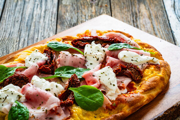Pinsa Romana with cooked ham, burrata cheese and sun dried tomatoes on wooden table

