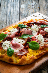 Pinsa Romana with cooked ham, burrata cheese and sun dried tomatoes on wooden table
