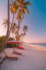 Beautiful tropical sunset coast, two sun beds, loungers, umbrella under palm trees. Closeup sand, sea horizon, colorful twilight sky, calm and relax. Peaceful romantic couple travel vacation landscape