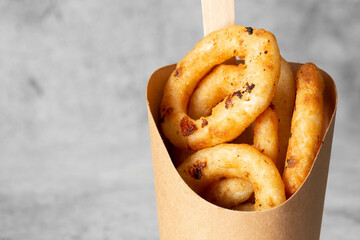 Battered onion rings takeaway in a cardboard carton with a wooden fork. Biodegradable plastic free...