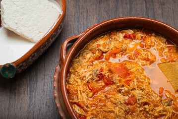Authentic mexican chicken tinga, typical mexican food prepared in a clay pot on a wooden table.