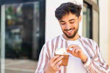 Handsome Arab man at outdoors holding wallet with money with happy expression
