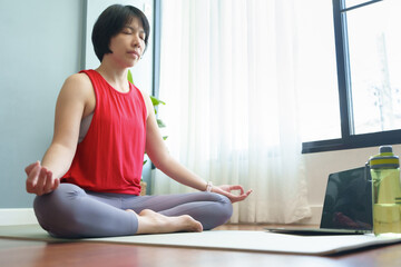 Asian Chinese woman sitting in yoga lotus position at home. Breathing, Working out, Meditation, wellness concept