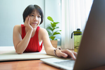 Obraz premium Asian chinese woman in sportwear lying on the floor using Laptop while doing yoga exercise at home. Typing on computer.