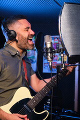 Singer and guitarist with headphones and microphone recording new album at a recording studio.