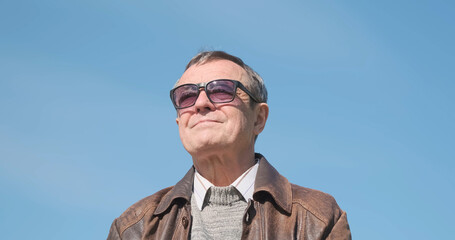 Stylish happy elderly man looks into the distance. Blue sky, low angle, portrait.