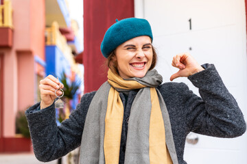 Brunette woman holding home keys at outdoors proud and self-satisfied