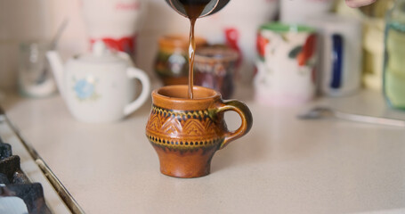 Man's hand copper cezve pours ready-made coffee from wand into ceramic cup. Process of making homemade coffee