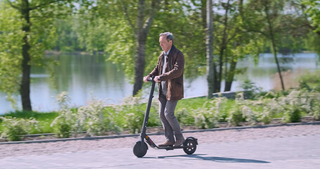 Man rides electric scooter in city park on spring day. Concept of electric transport in city, an environmentally friendly mode of transport.