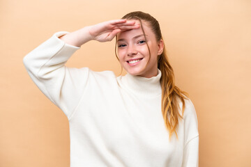 Young caucasian woman isolated on beige background saluting with hand with happy expression