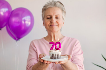 Elderly smiling cool happy woman 70s hold birthday cake with candle