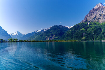 Scenic mountain panorama with Lake Lucerne in the foreground and Swiss village Flüelen in the background on a sunny spring day. Photo taken May 22nd, 2023, Lake Lucerne, Switzerland.