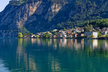 Fototapeta na wymiar Scenic view of Swiss village of Flüelen with beautiful reflections in water on a sunny spring morning. Photo taken May 22nd, 2023, Flüelen, Canton Uri, Switzerland.