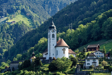 Fototapeta na wymiar Mountain panorama at Swiss village of Flüelen on a sunny spring morning with church tower on a sunny spring morning. Photo taken May 22nd, 2023, Flüelen, Canton Uri, Switzerland.