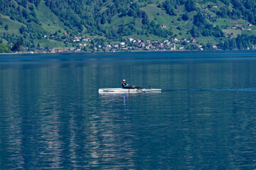 Fototapeta na wymiar Man in rowing boat on Lake Lucerne on a sunny spring morning. Photo taken May 22nd, 2023, Flüelen, Canton Uri, Switzerland.