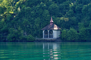 Fototapeta na wymiar Famous Tell's Chapel at lakeshore of Lake Uri on a sunny spring day with woodland in the background. Photo taken May 22nd, 2023, Sisikon, Canton Uri, Switzerland.