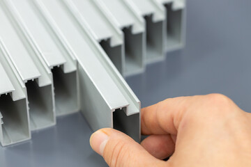 Aluminum profiles on a gray background, a hand extending an aluminum component, a material used in...