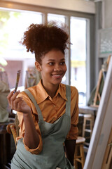 Smiling African American female artist creating masterpiece, painting picture with brush on canvas...